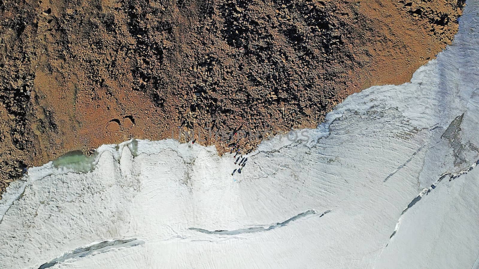 People on the top of a snowy mountain. Top view from a drone. Huge rocks covered with snow, climbers stand on top of the peak. Extreme rest. Steep slopes where there may be an avalanche. Highest peak