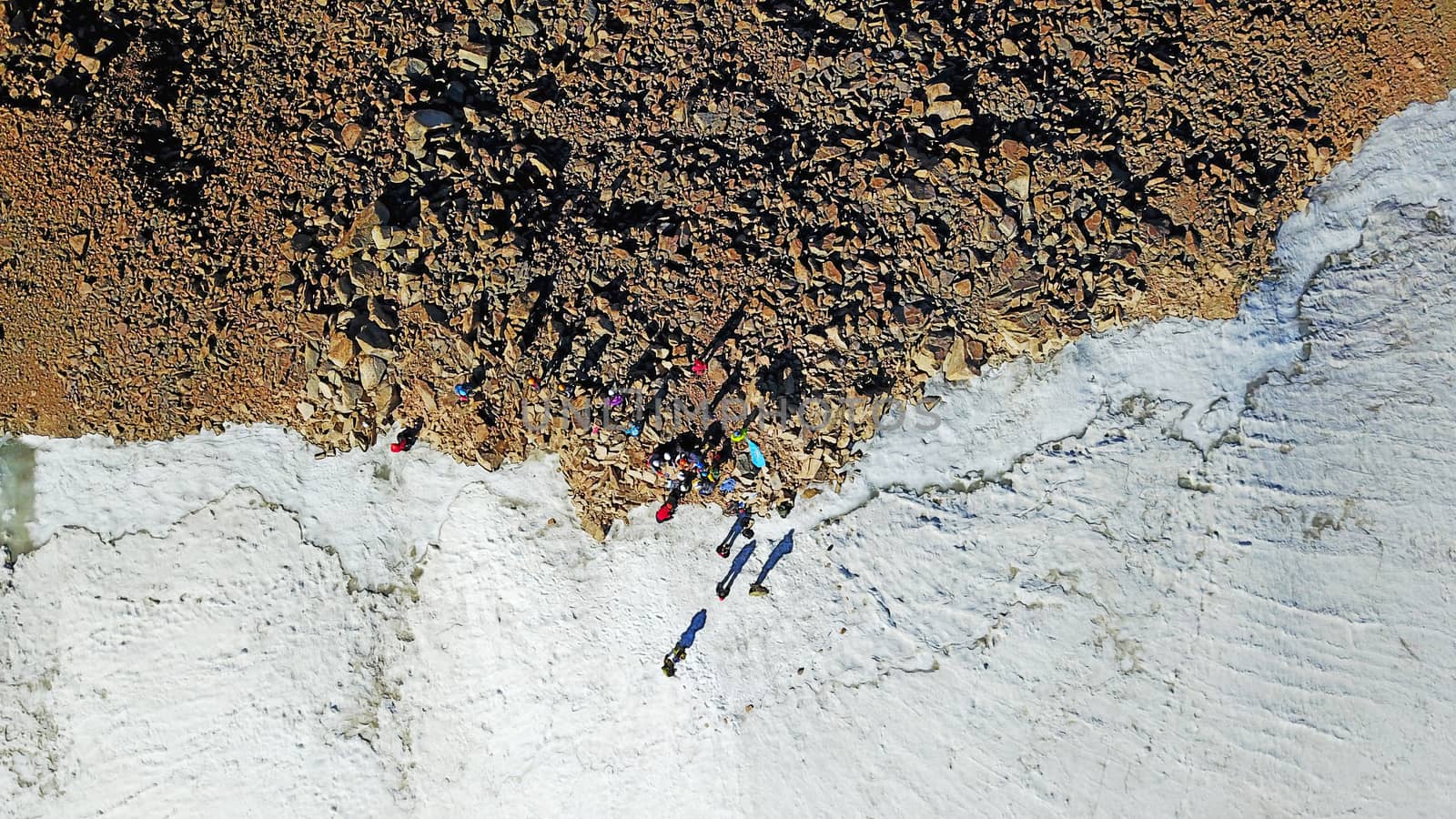 People on the top of a snowy mountain. Top view from a drone. Huge rocks covered with snow, climbers stand on top of the peak. Extreme rest. Steep slopes where there may be an avalanche. Highest peak