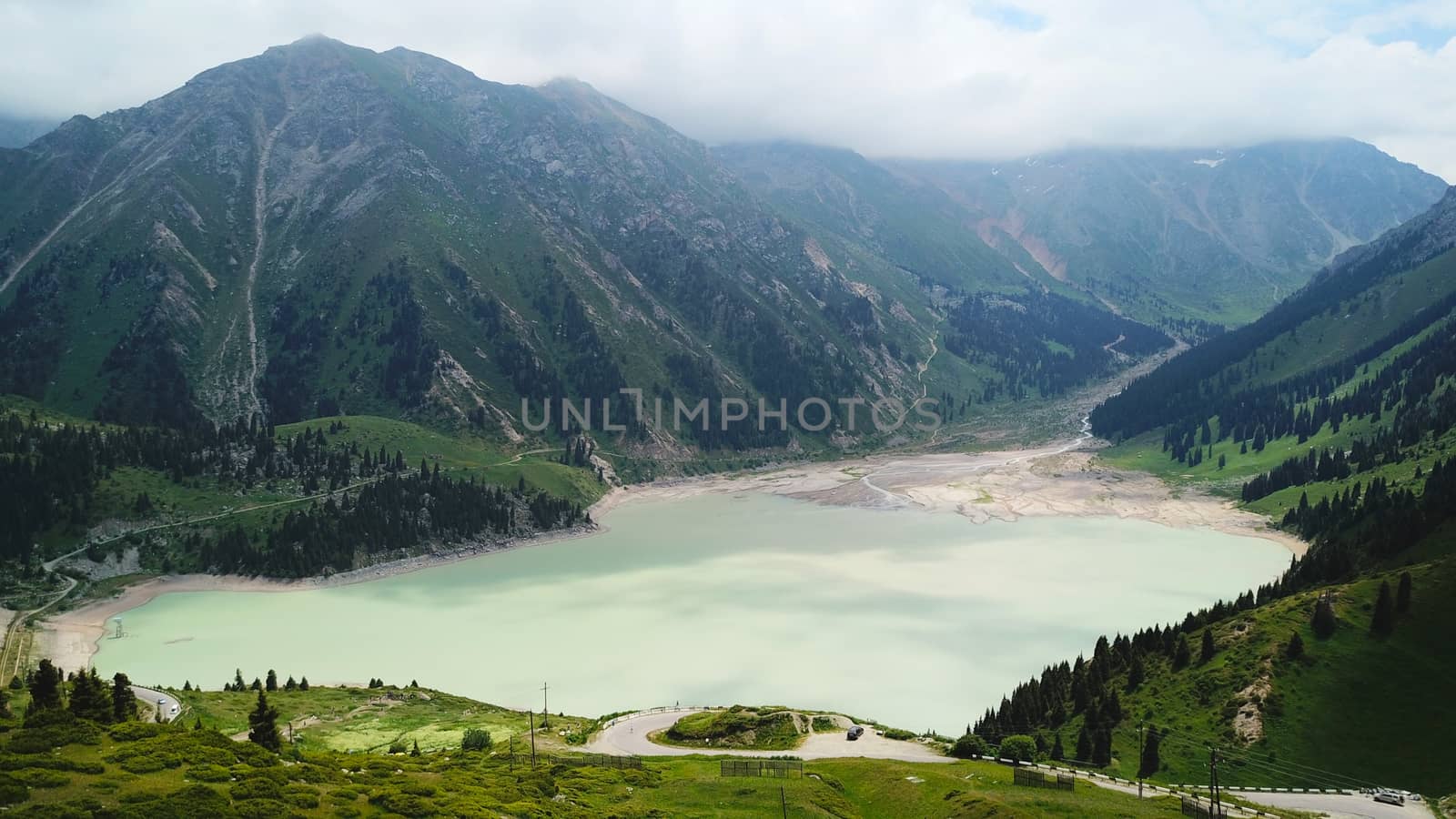 Big Almaty lake in the mountains. Green hills, flowers and fields. White clouds over the mountains. Mountain lake. In places there are stones. Protected place of nature, reserve of TRANS-ili Alatau