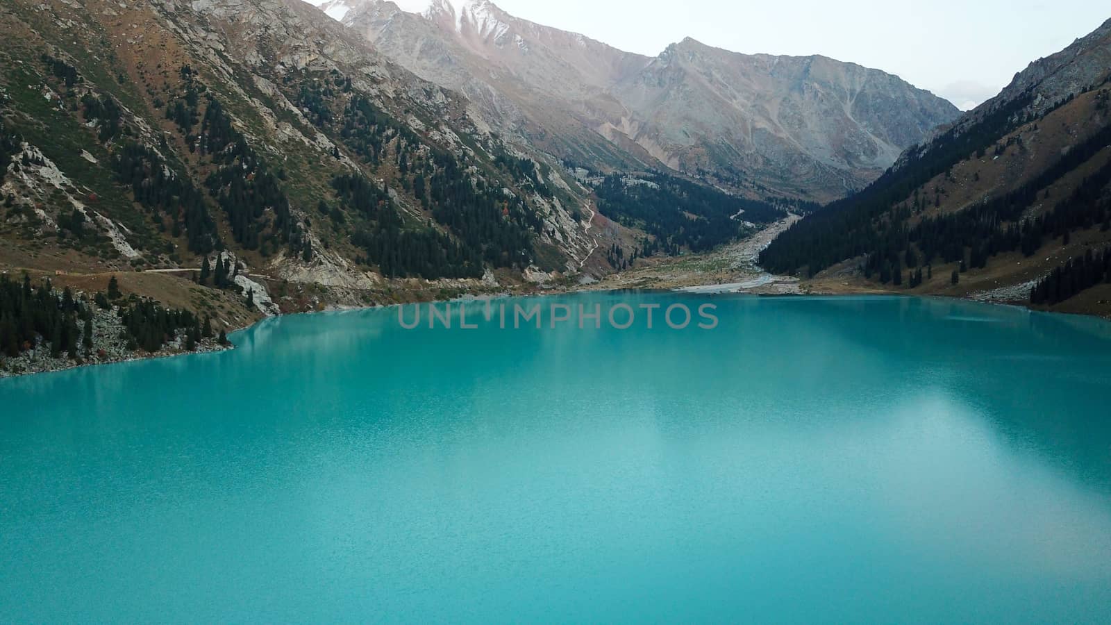 Big Almaty lake in the mountains. Green hills, flowers and fields. White clouds over the mountains. Mountain lake. In places there are stones. Protected place of nature, reserve of TRANS-ili Alatau