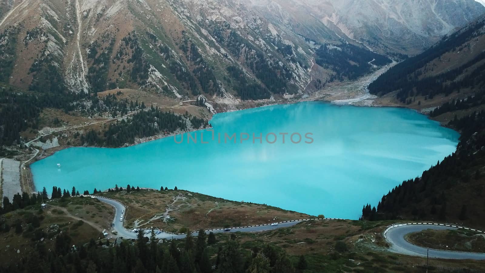 Big Almaty lake in the mountains. Green hills, flowers and fields. White clouds over the mountains. Mountain lake. In places there are stones. Protected place of nature, reserve of TRANS-ili Alatau