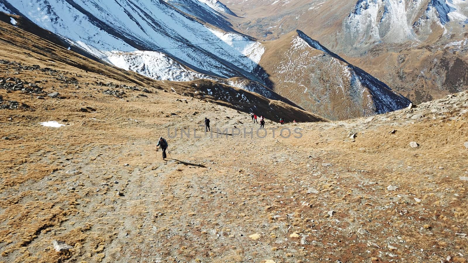 A group of tourists stands on the mountainside. There is snow in places. Very large stones on the sides. Blue sky with white clouds. Top view from the throne. Mountainous area of Kazakhstan.