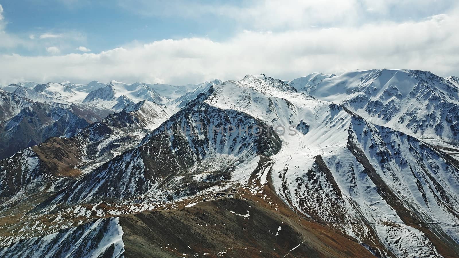 Mountain tops covered with snow. View from a drone. Huge rocks lie on the steep slopes of the mountains. Snow-capped peaks can be seen in the distance, sometimes flashing the city in the smog.