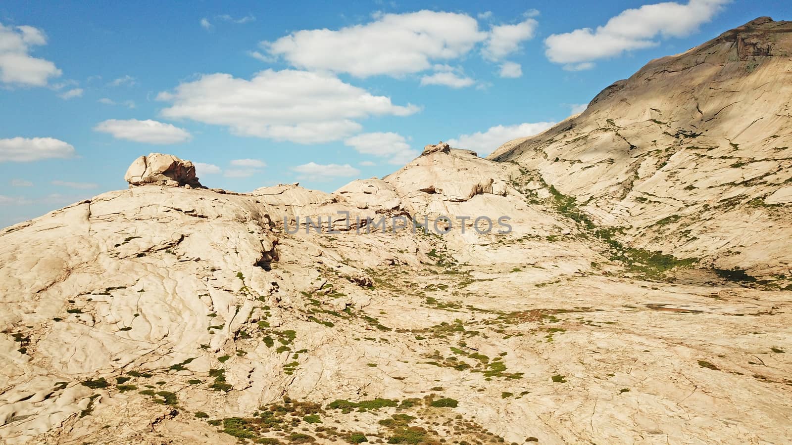 Huge rocks from lava. A former volcano. Bektau-ATA Tract. Large rocks, rifts, cracks, and mountains. In places, grass grows and water is visible. Unusual Martian landscape. Blue sky and clouds.