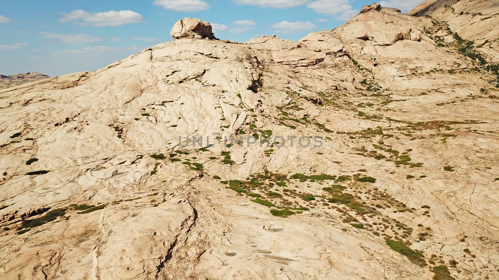 Huge rocks from lava. A former volcano. Bektau-ATA Tract. Large rocks, rifts, cracks, and mountains. In places, grass grows and water is visible. Unusual Martian landscape. Blue sky and clouds.