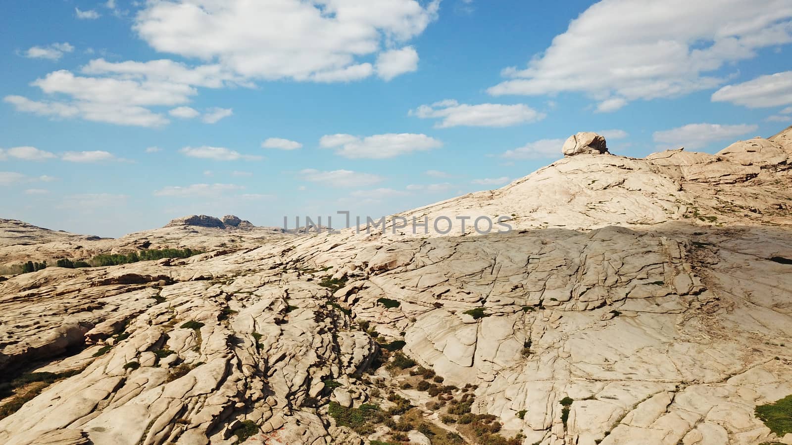 Huge rocks from lava. A former volcano. Bektau-ATA Tract. Large rocks, rifts, cracks, and mountains. In places, grass grows and water is visible. Unusual Martian landscape. Blue sky and clouds.