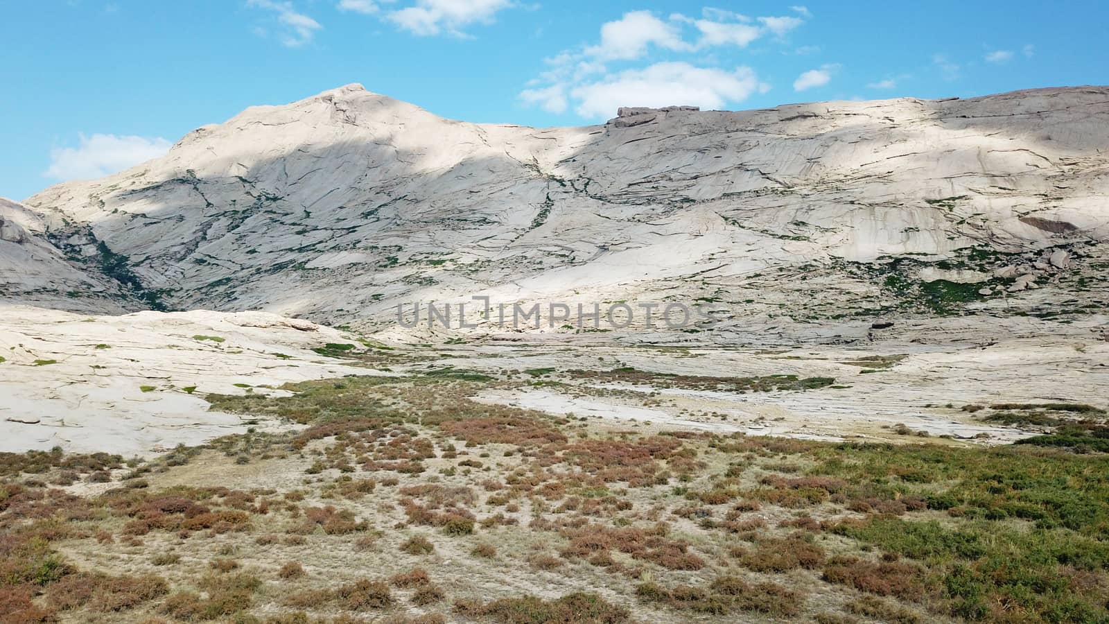 Huge rocks from lava. A former volcano. Bektau-ATA Tract. Large rocks, rifts, cracks, and mountains. In places, grass grows and water is visible. Unusual Martian landscape. Blue sky and clouds.