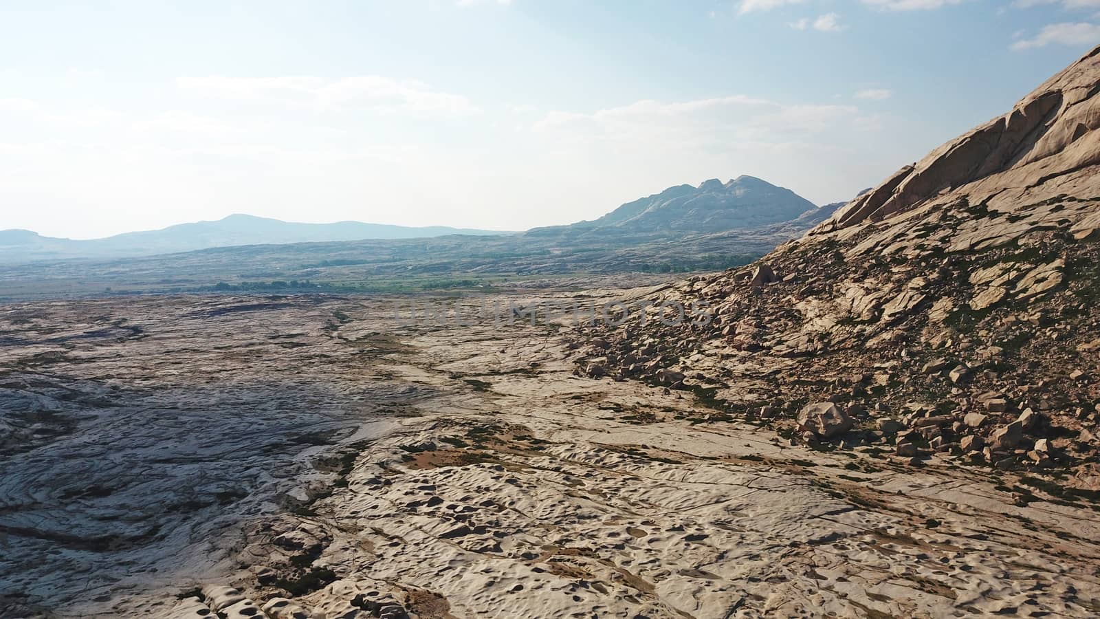 Huge rocks from lava. A former volcano. Bektau-ATA Tract. Large rocks, rifts, cracks, and mountains. In places, grass grows and water is visible. Unusual Martian landscape. Blue sky and clouds.