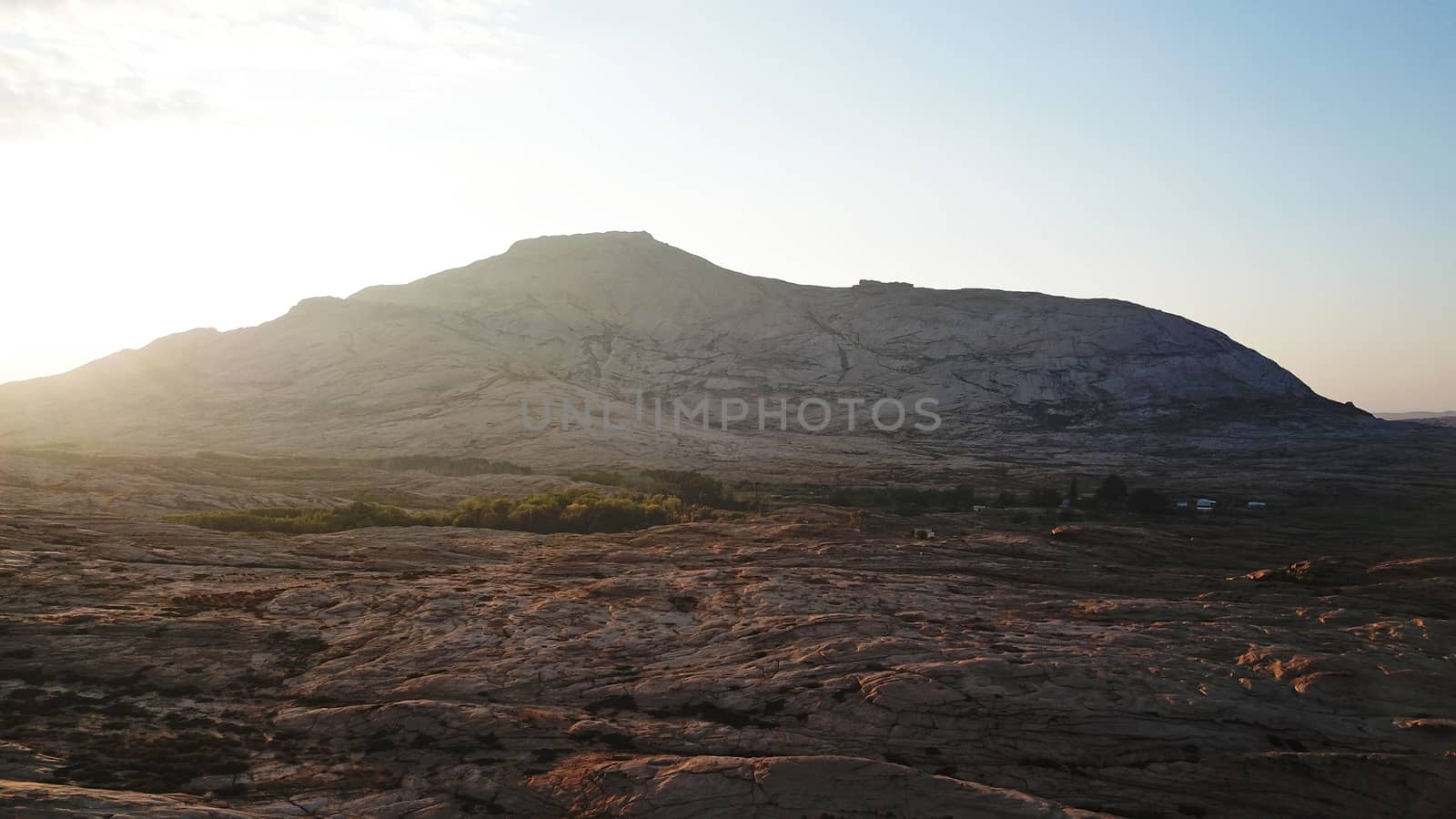 Dawn over frozen lava and mountains. Huge rocks and a gorge cast a shadow from the sun. Grass and trees grow in places. Houses are visible. Clouds in sky and bright rays of the sun. Beautiful gorge.