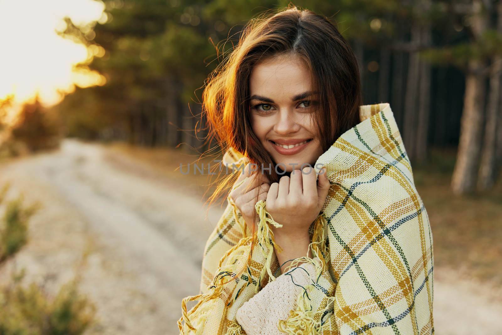 Smiling woman covering herself with a plaid looking forward on nature. High quality photo