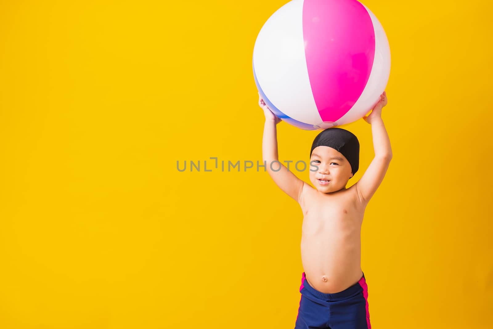 Summer vacation concept, Portrait Asian happy cute little child boy smiling in swimsuit hold beach ball, Kid having fun with inflatable ball in summer vacation, studio shot isolated yellow background