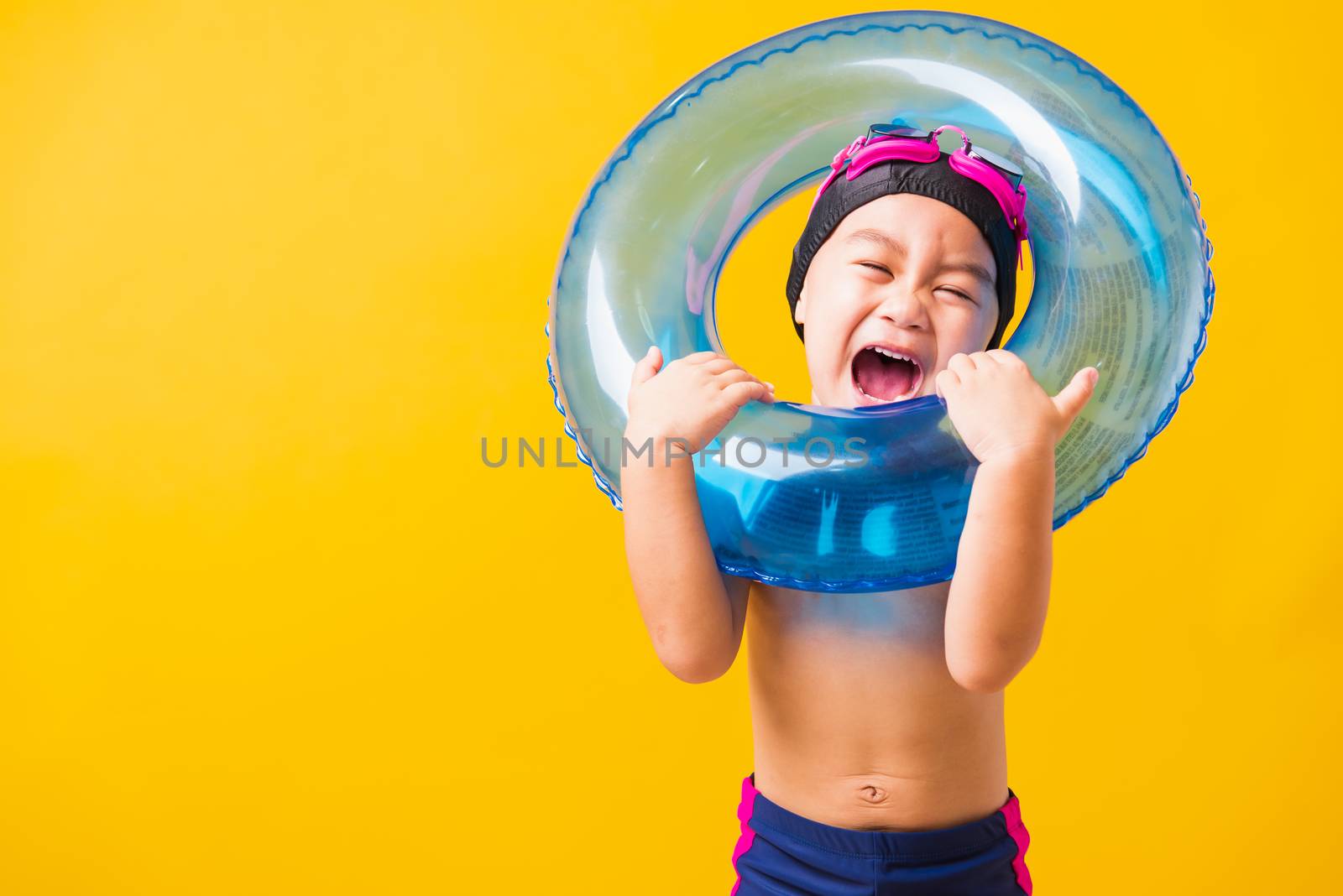 Summer vacation concept, Portrait Asian happy cute little child boy wear goggles and swimsuit hold blue inflatable ring, Kid having fun on summer vacation, studio shot isolated yellow background