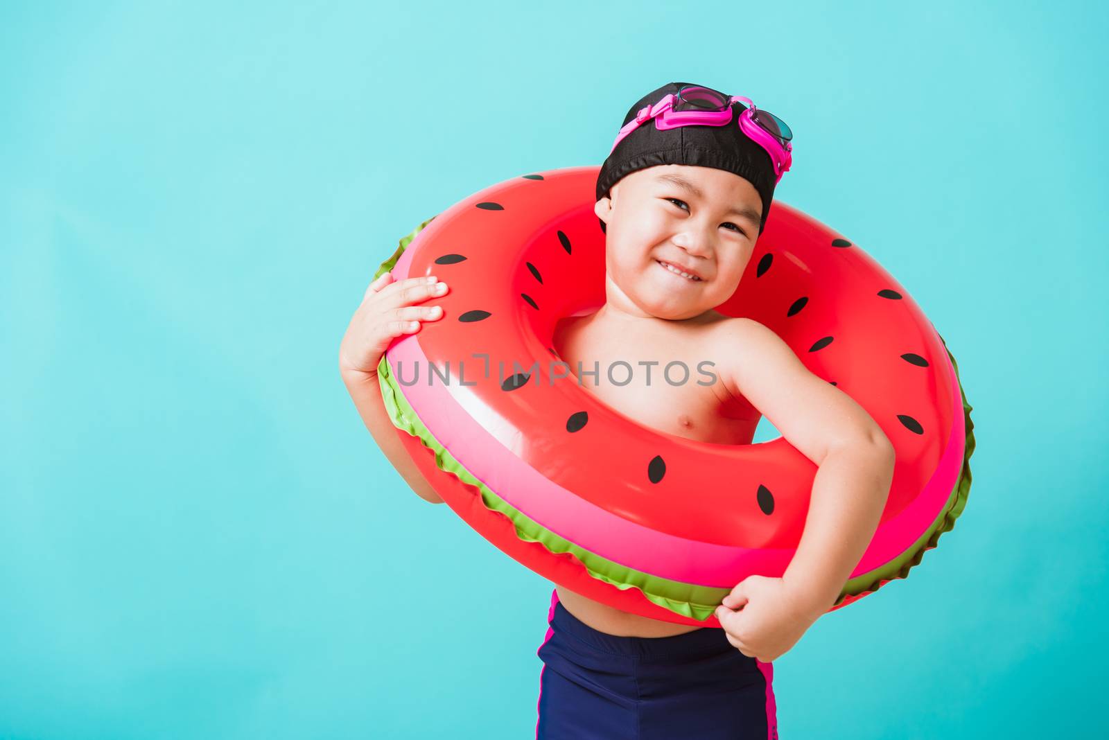 Summer vacation concept, Portrait Asian happy cute little child boy wear goggles and swimsuit hold watermelon inflatable ring, Kid having fun on summer vacation, studio shot isolated blue background