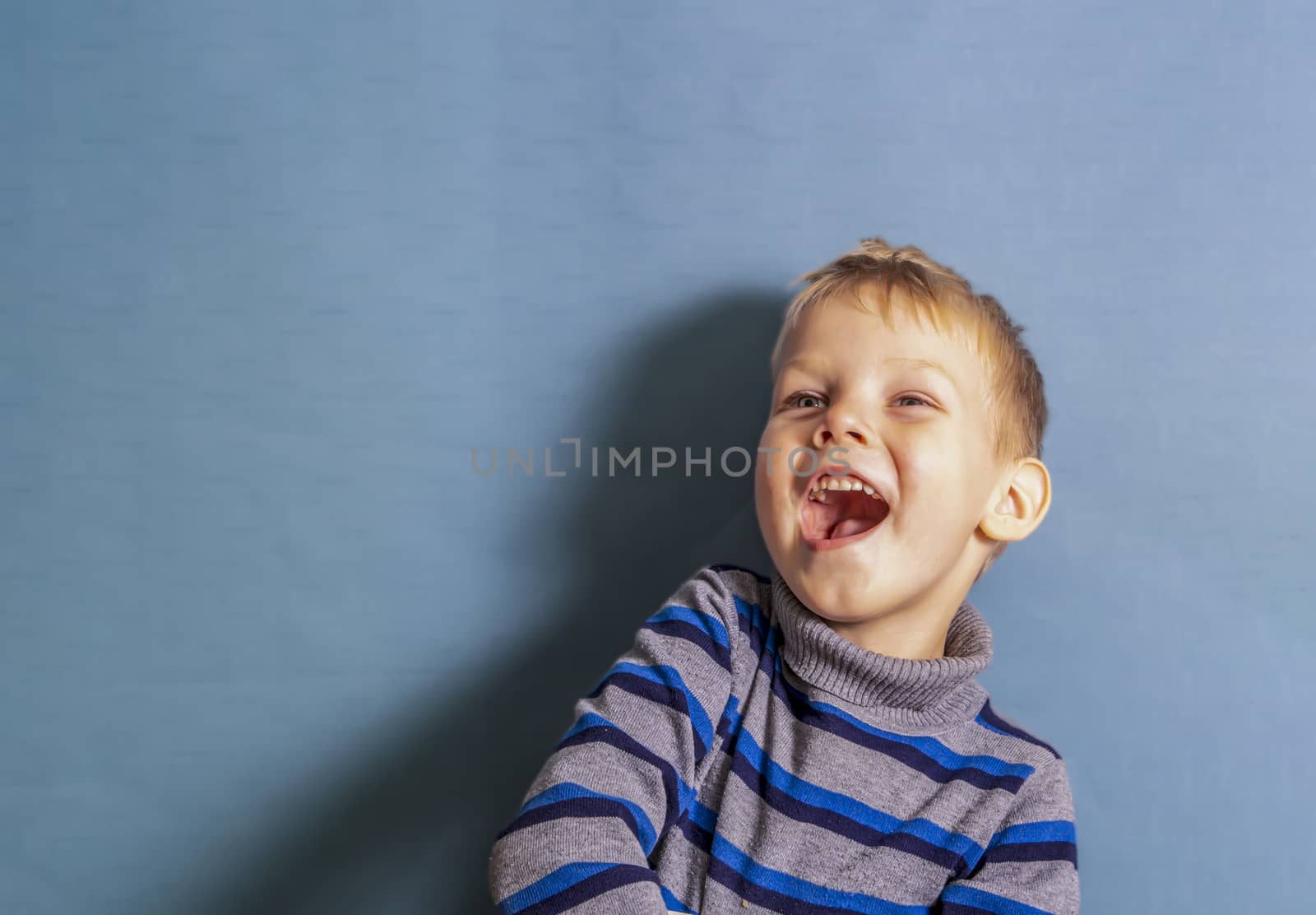 a boy in a gray striped jacket laughs when he sees something in front of him, a copy space. by Akmenra