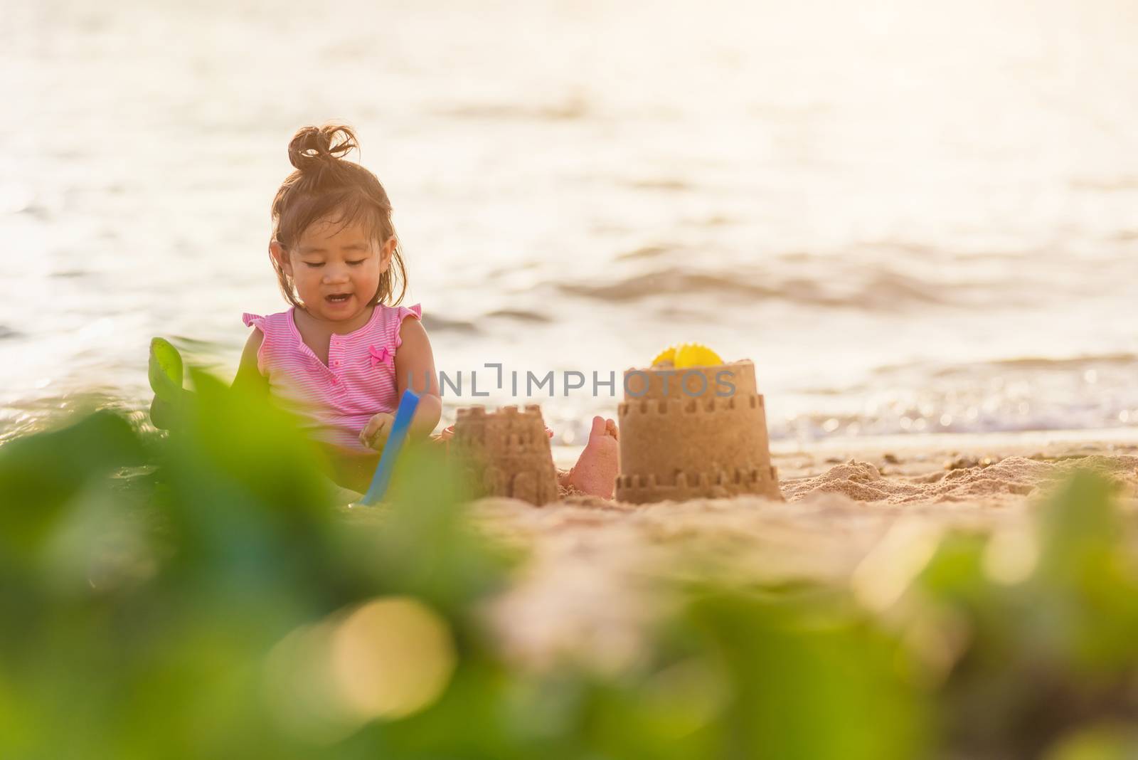 Happy fun Asian child cute little girl playing sand with toy sand tools at a tropical sea beach in holiday summer on sunset time, tourist trip concept
