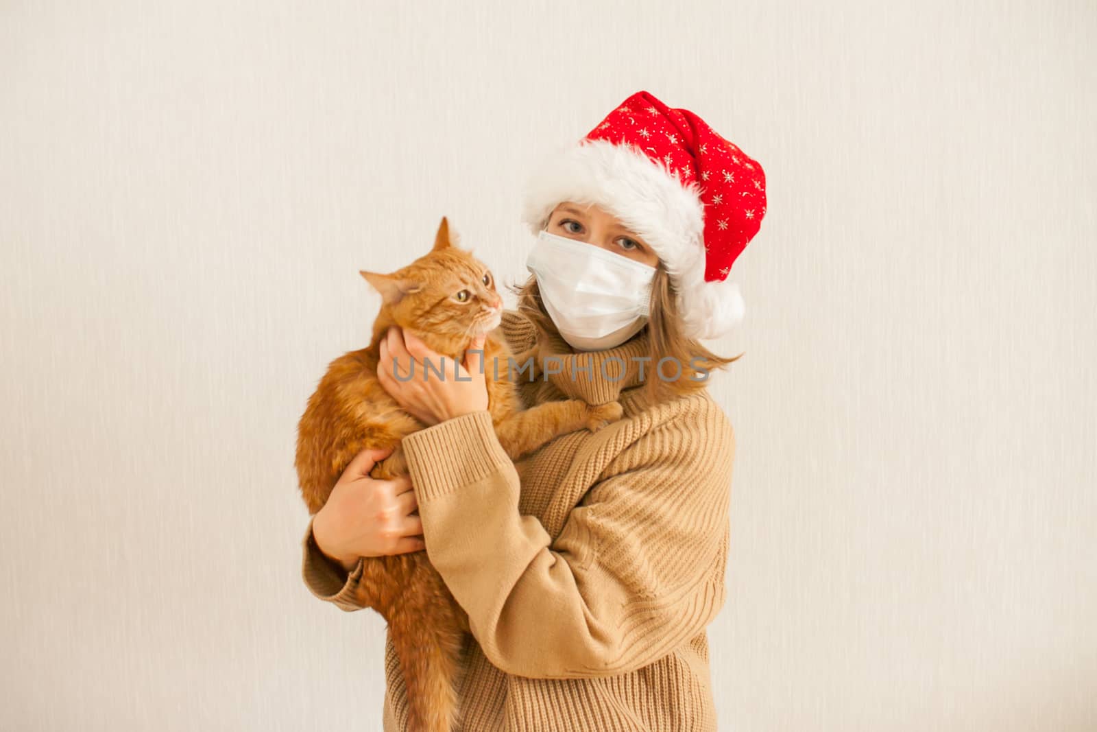 girl in a santa hat and a medical protective mask holds a fat ginger cat in her hands. New Year 2021 by malyshkamju