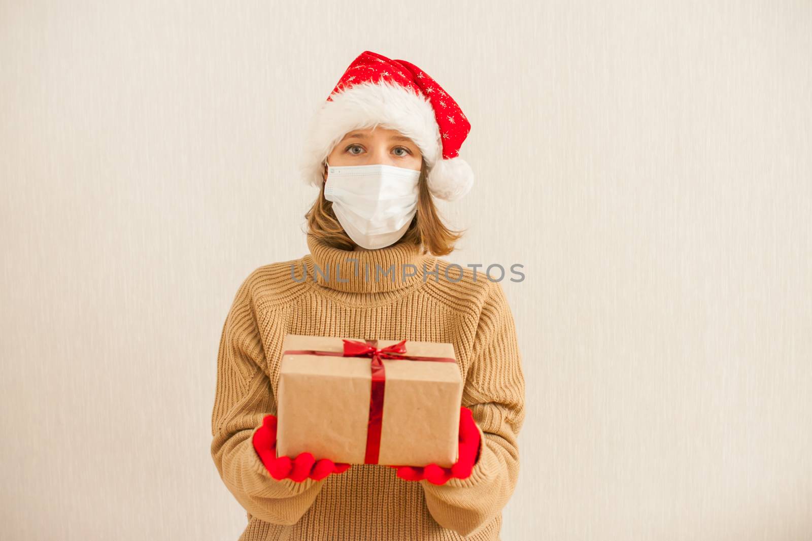 a girl in a santa hat and a medical protective mask holds gifts in her hands. New Year 2021