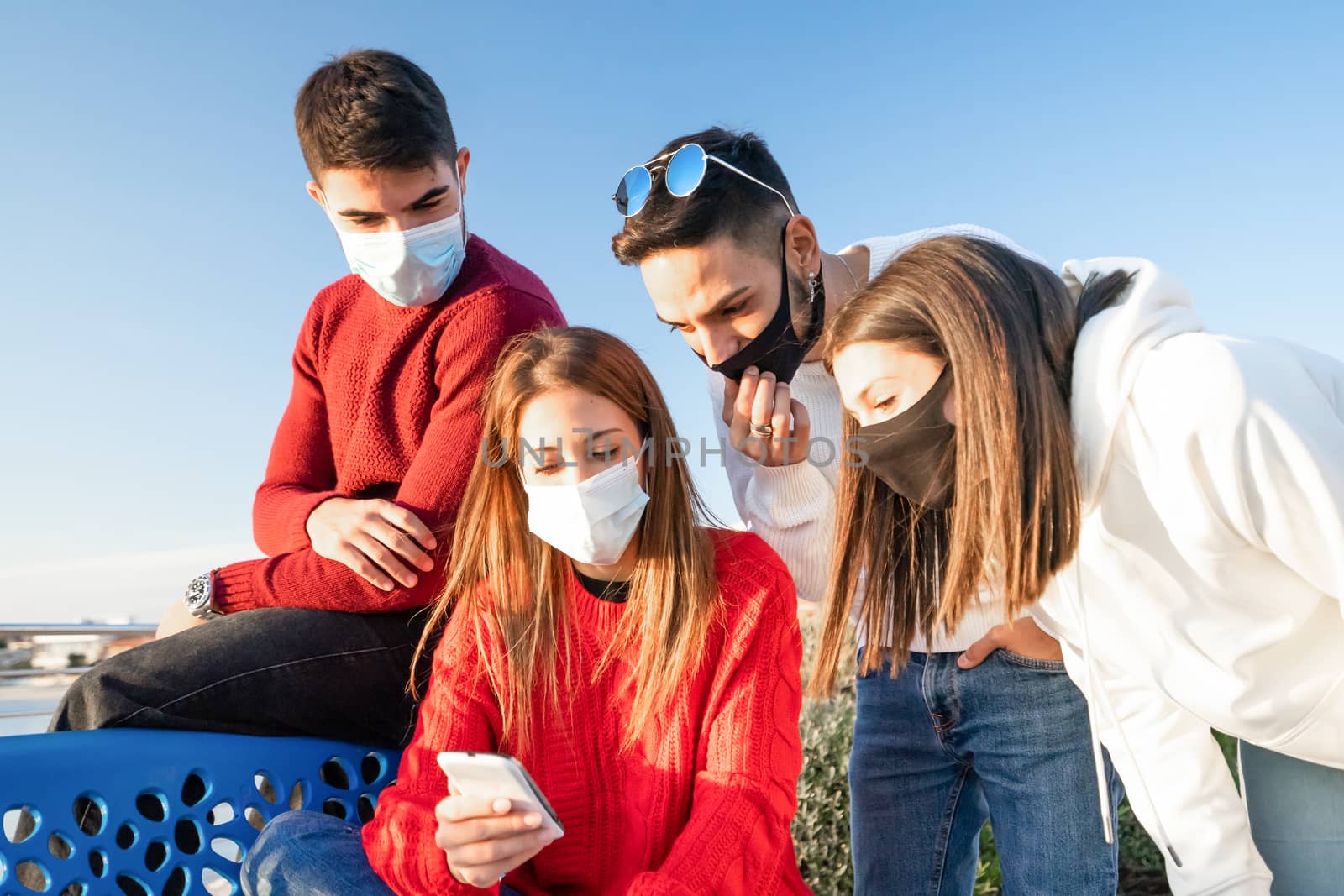 Group of young friends looking at the smartphone outdoor wearing Coronavirus safe protection mask - Two heterosexual couples of traveler searching online with cell for their winter vacation