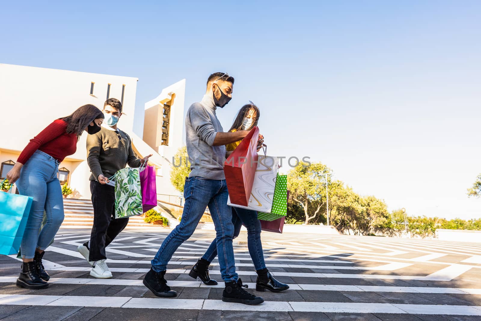 Young friends group outdoor in the city square walking satisfied of purchases wearing Coronavirus safe protection mask - Beautiful people with casual clothing having fun outdoor with shopping bags