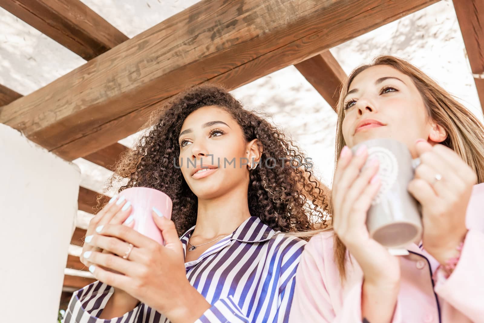 Beauty and diversity: mixed race couple in pajama view from bottom holding tea mug in hand - Caucasian woman and her Hispanic girlfriend just woke up looking toward horizon - Focus on brunette on left