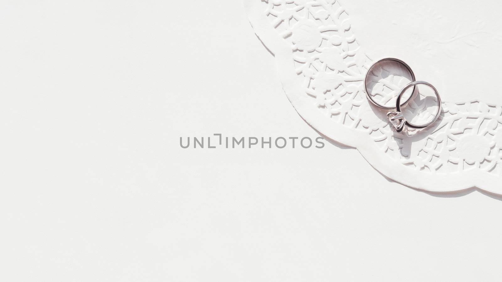 Top view on wedding and engagement rings with diamond on laced napkin. Symbol of love and marriage on white background. Sunlight on white background.