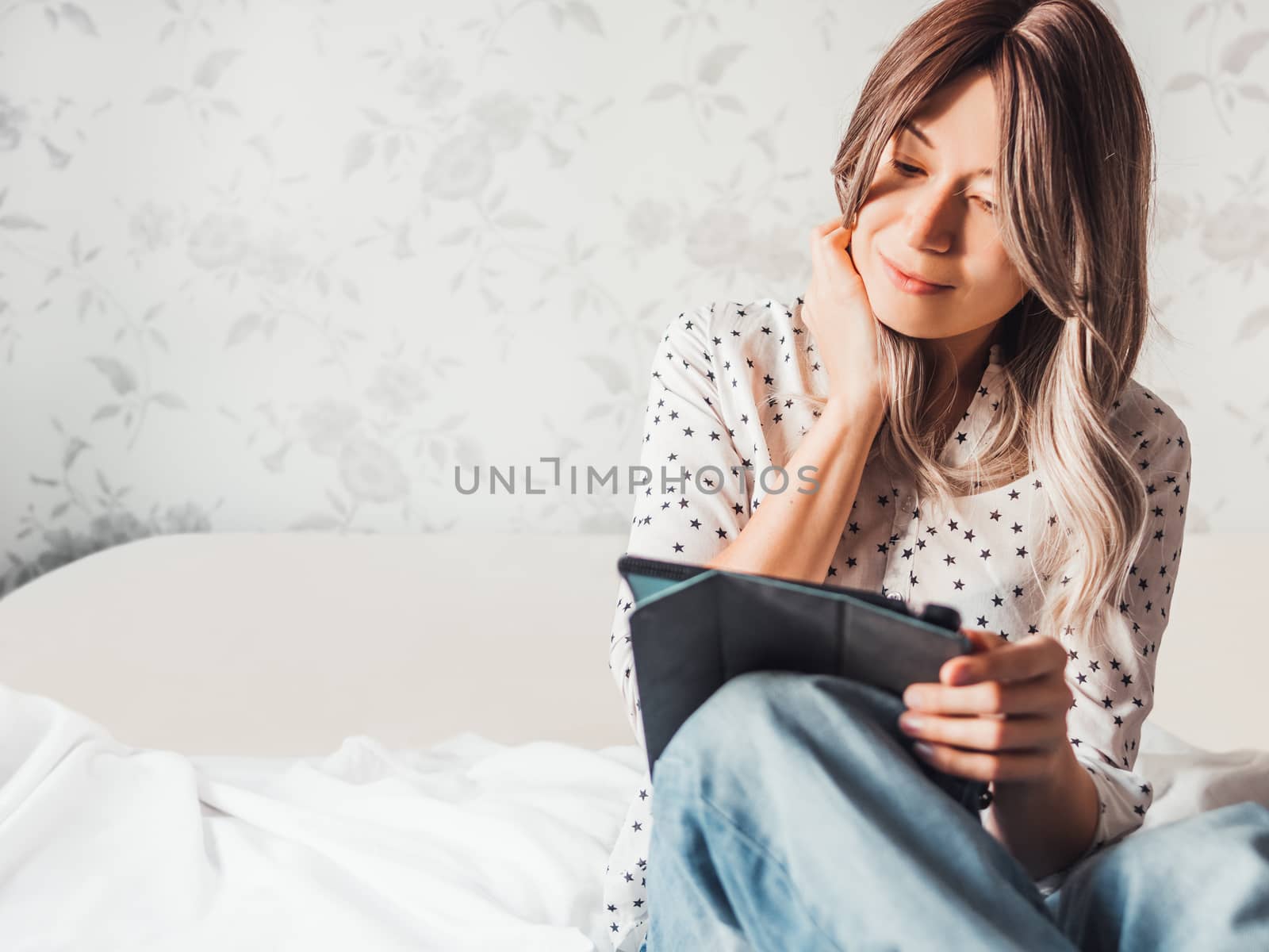 Woman sits on bed with tablet PC. She watches online TV series. Online video call or conference, distance learning, remote education. Self isolation during quarantine.