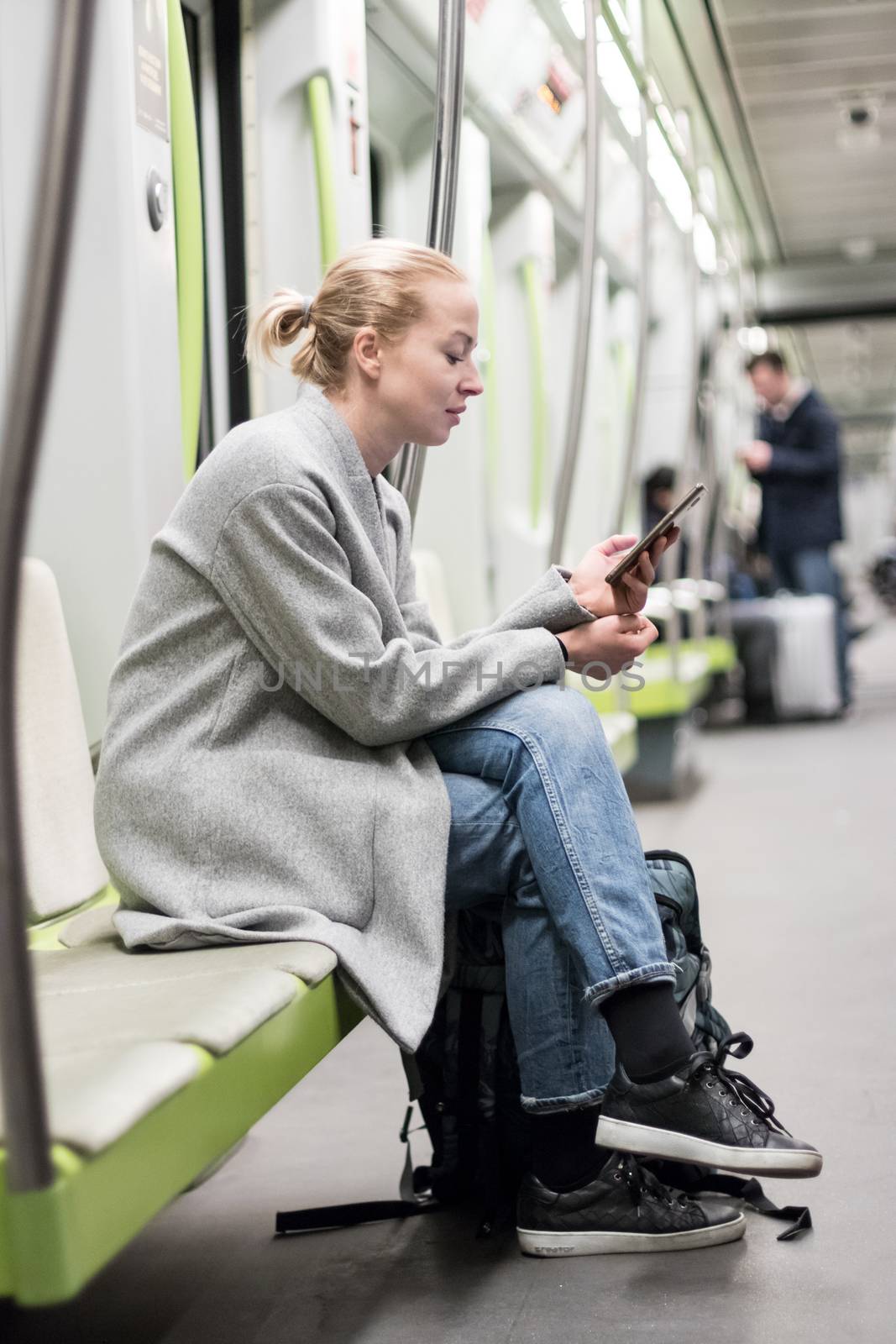 Portrait of lovely girl typing message on mobile phone in almost empty public subway train. Staying at home and social distancing recomented due to corona virus pandemic outbreak by kasto