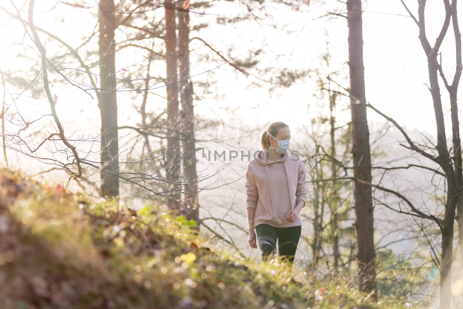 Portrait of caucasian sporty woman wearing a medical protection face mask while walking in the forest. Corona virus, or Covid-19, is spreading all over the world.