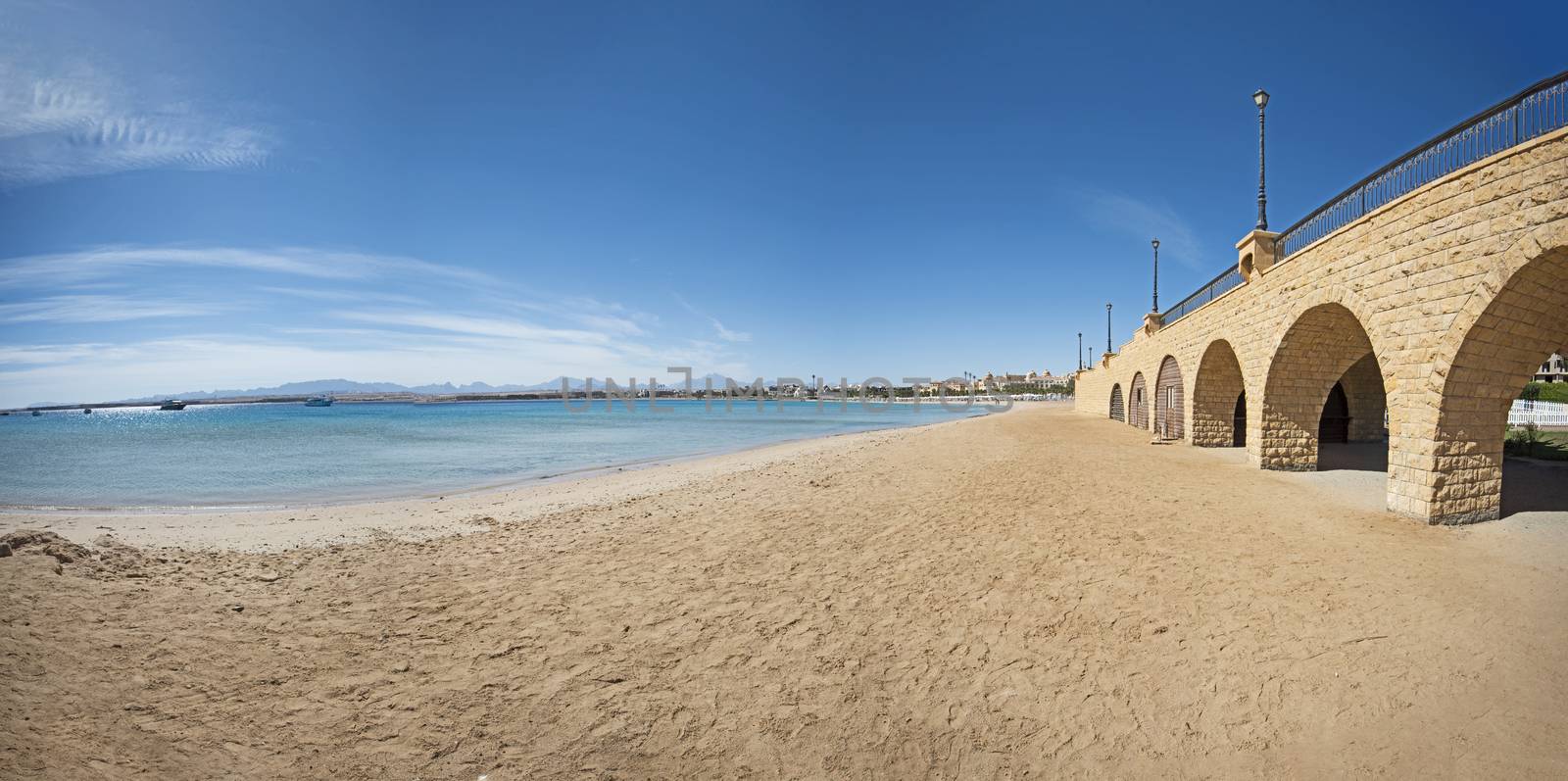 View across an empty tropical beach with stone bridge and arches by paulvinten