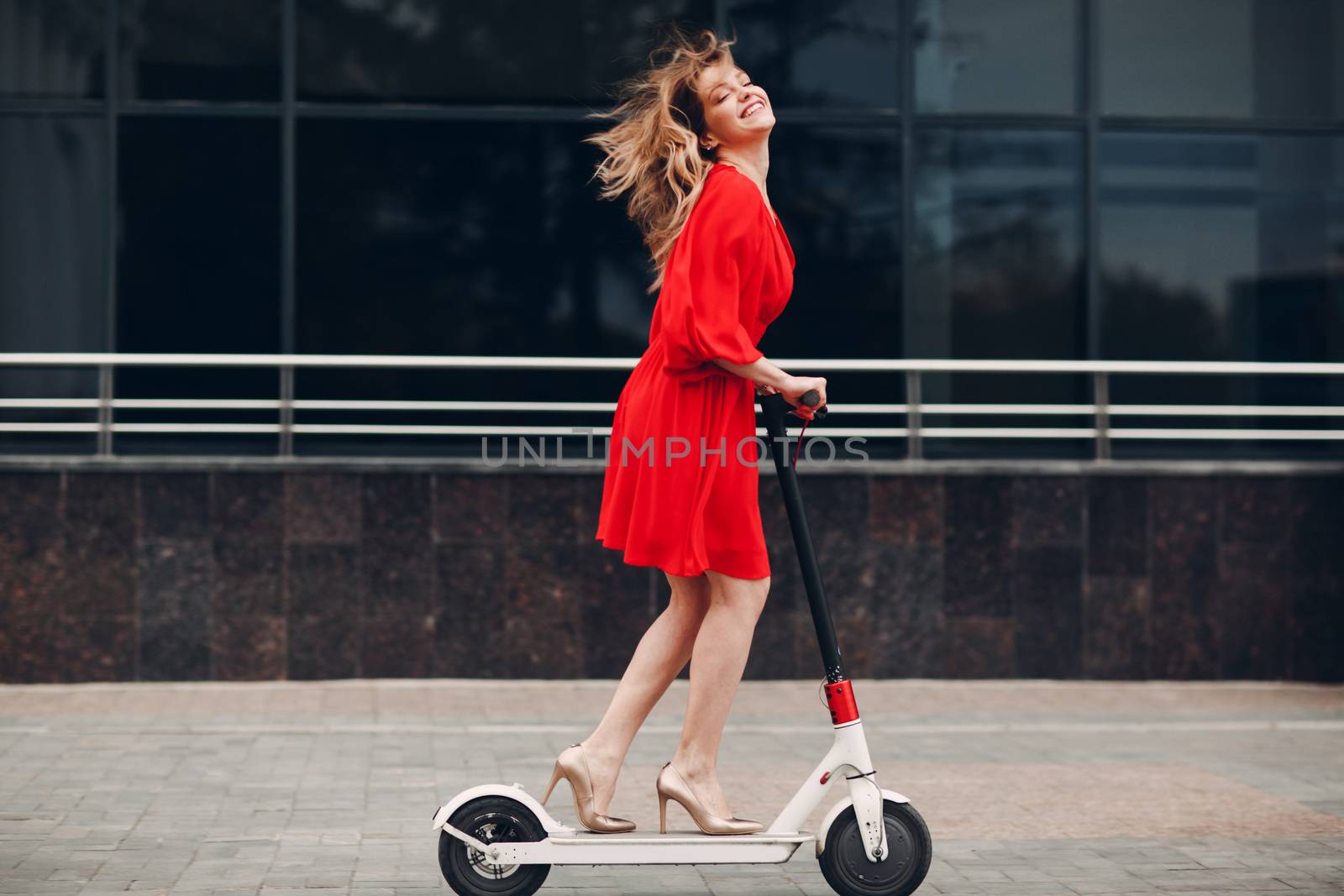 Young woman riding electric scooter in red dress at the city.