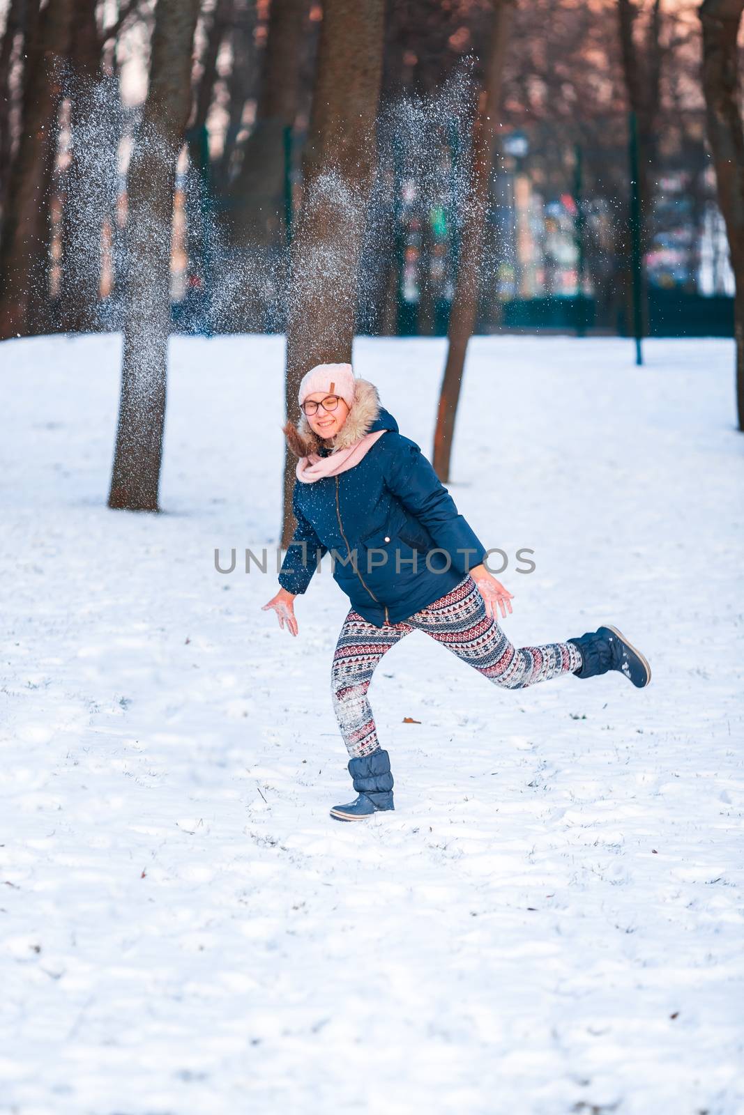 Happy teenage girl having a snowball fight, ready to throw a snowball, playing snowballs in winter park