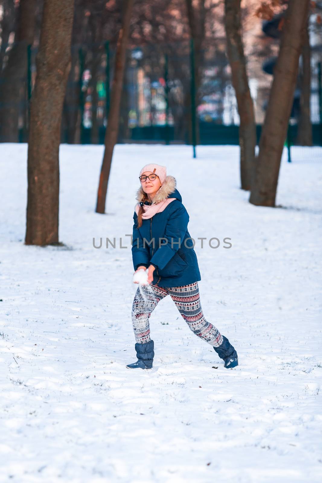 Happy teenage girl having a snowball fight, ready to throw a snowball, playing snowballs in winter park