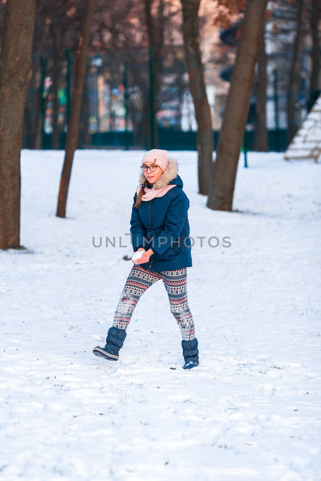 Happy teenage girl having a snowball fight, ready to throw a snowball, playing snowballs in winter park