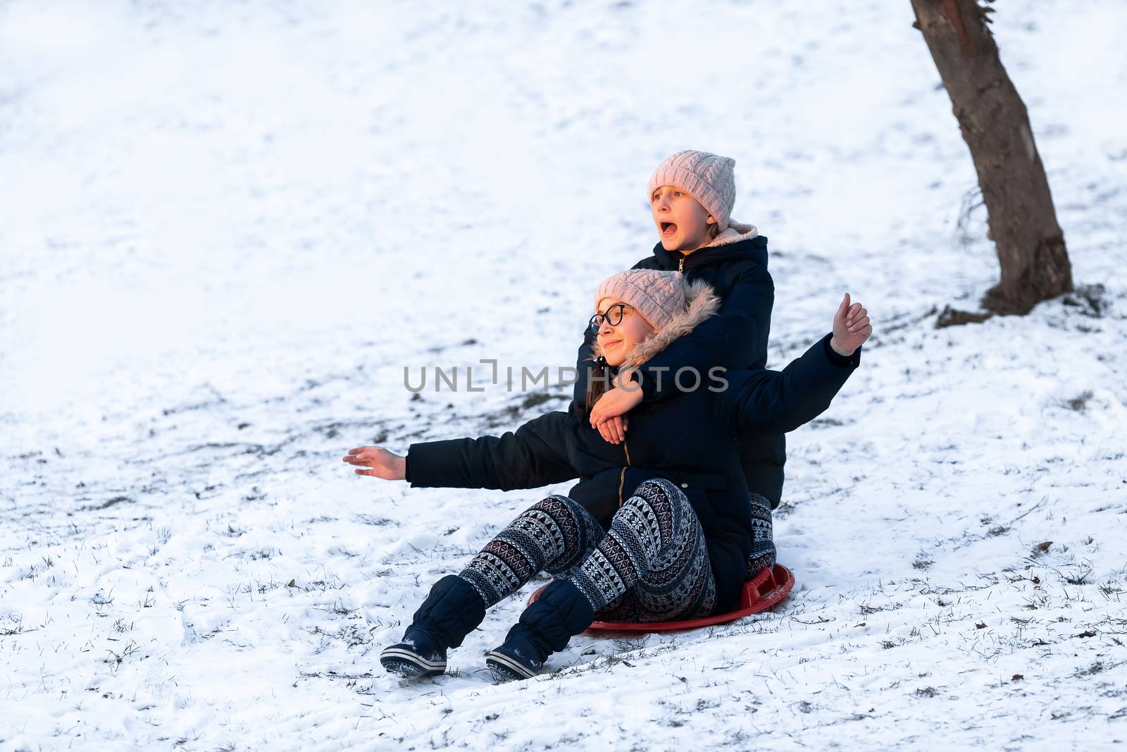 Little girls sliding from the hill in winter park