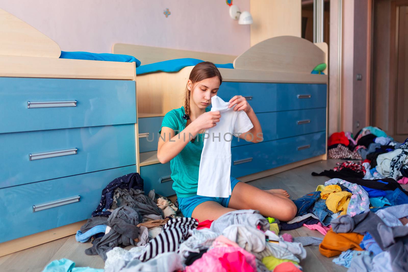 Beautiful teenage girl folding her clothes in a messy bedroom