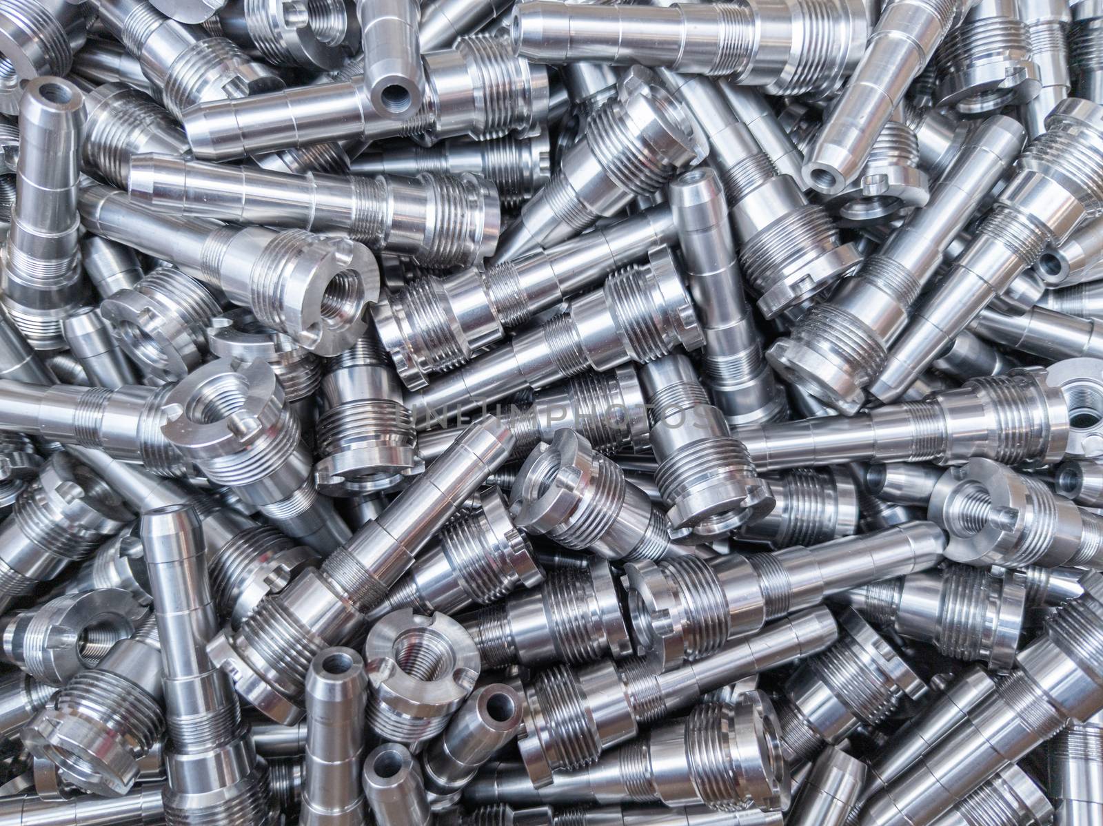 Full frame background of pile of shiny long steel parts, clean steel rods after fine cnc turning - laying chaotically with selective focus and blur.