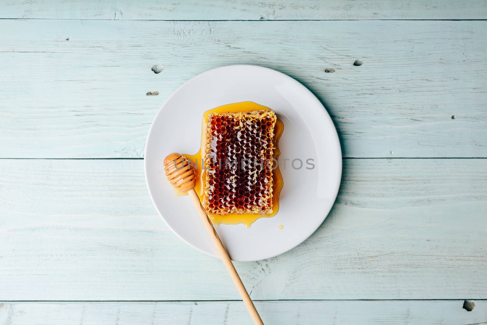 Top view of delicious yummy honeycomb on bright plate with honey dipper over light wooden background