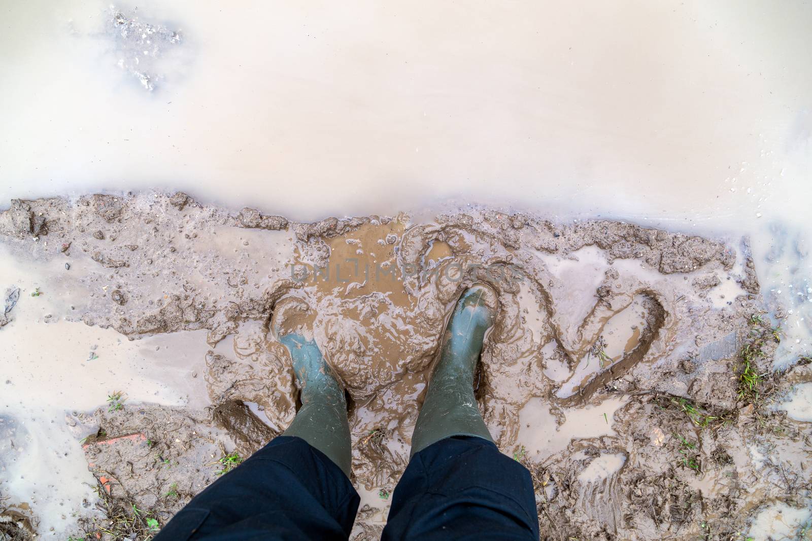 feet in green rubber boots stands in wet brown mud puddle, directly above first person gonzo view