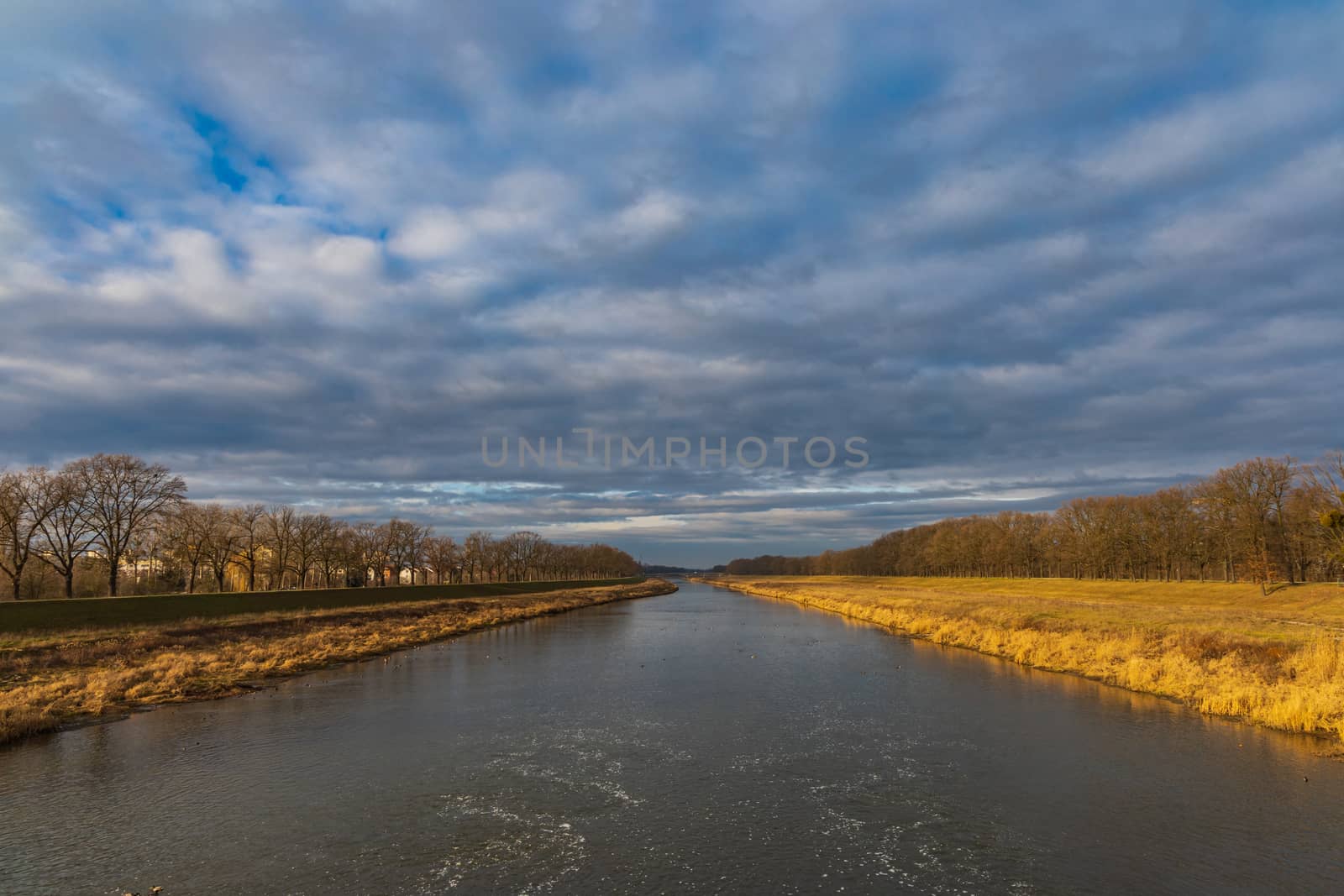 Cloudy landscape of river between yellow coasts and trees