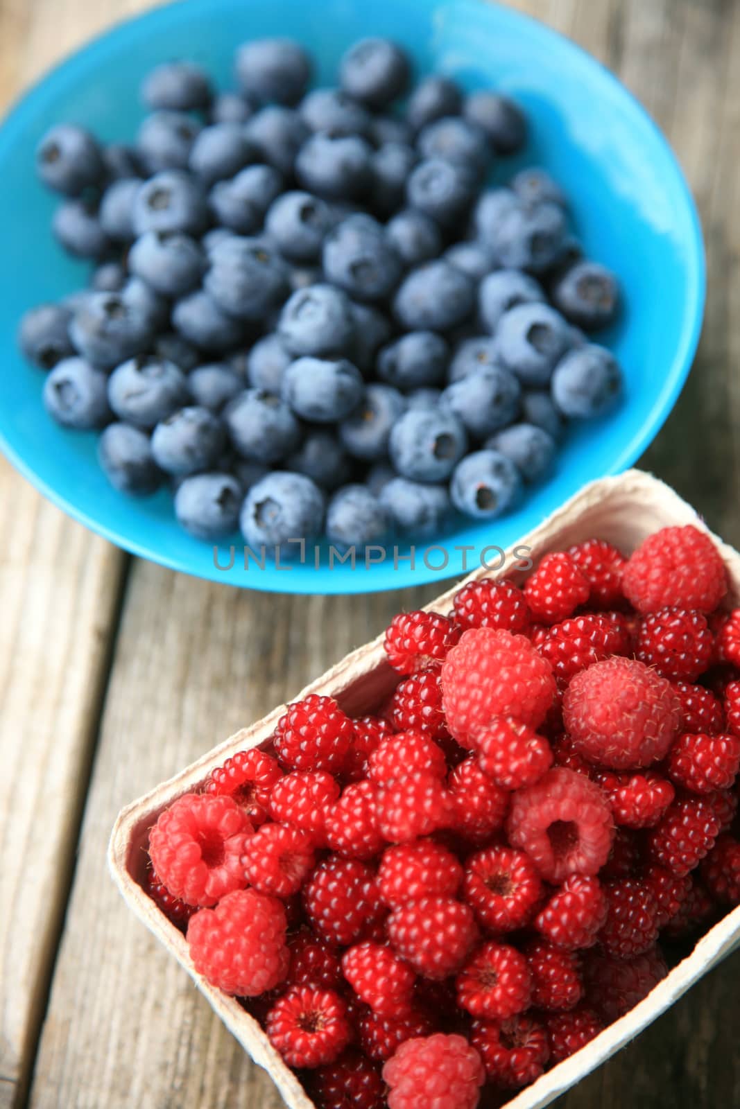 Blueberries in a blue glass bowl and raspberries in a paper box