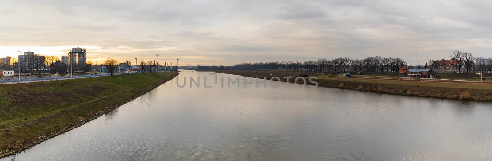 Cloudy panorama of Odra river between green coasts of city at sunset