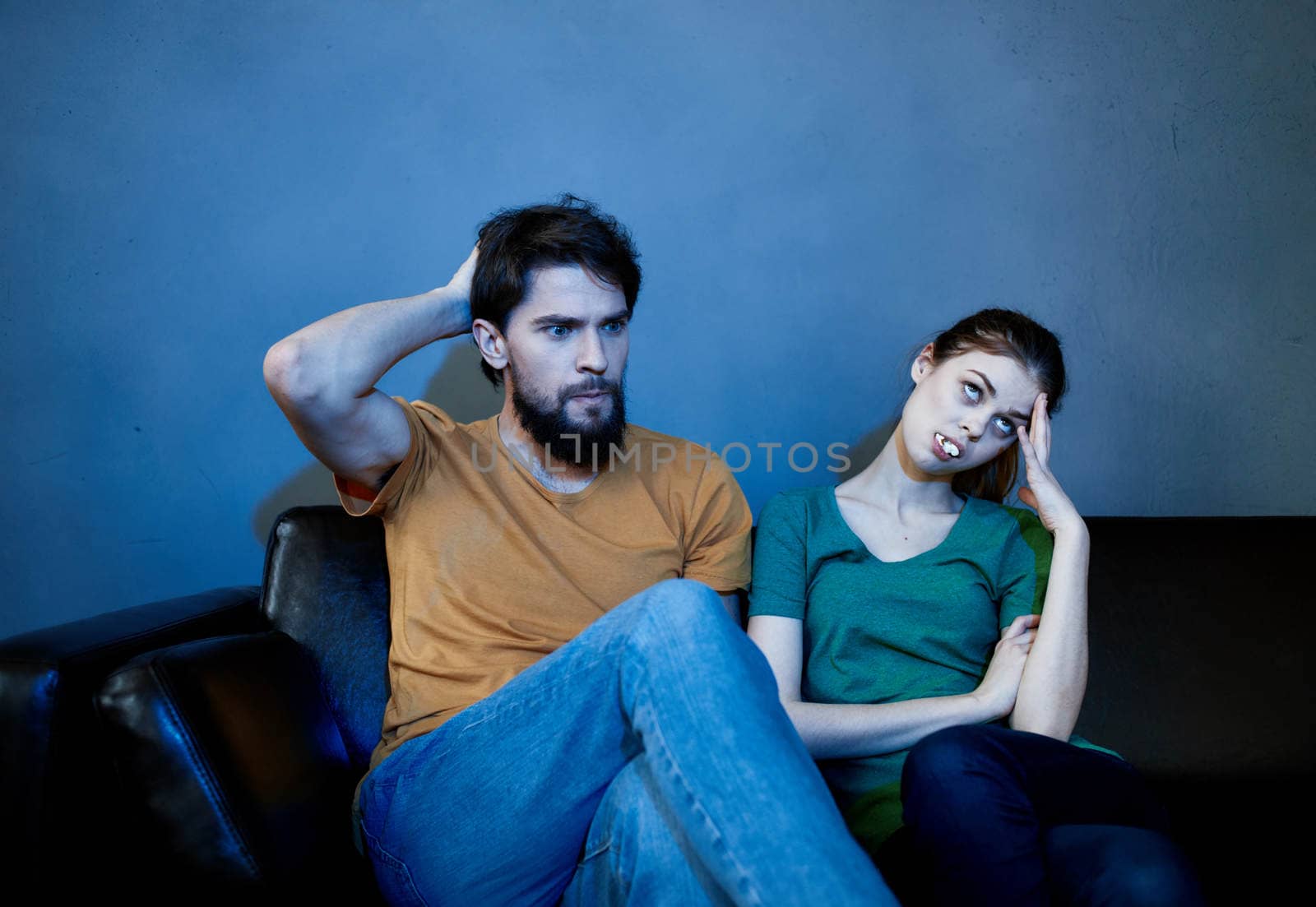 Cheerful man and emotional woman on a black sofa indoors in the evening watching TV by SHOTPRIME