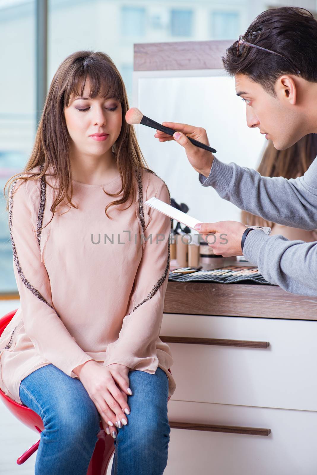 Man doing make-up for cute woman in beauty salon by Elnur