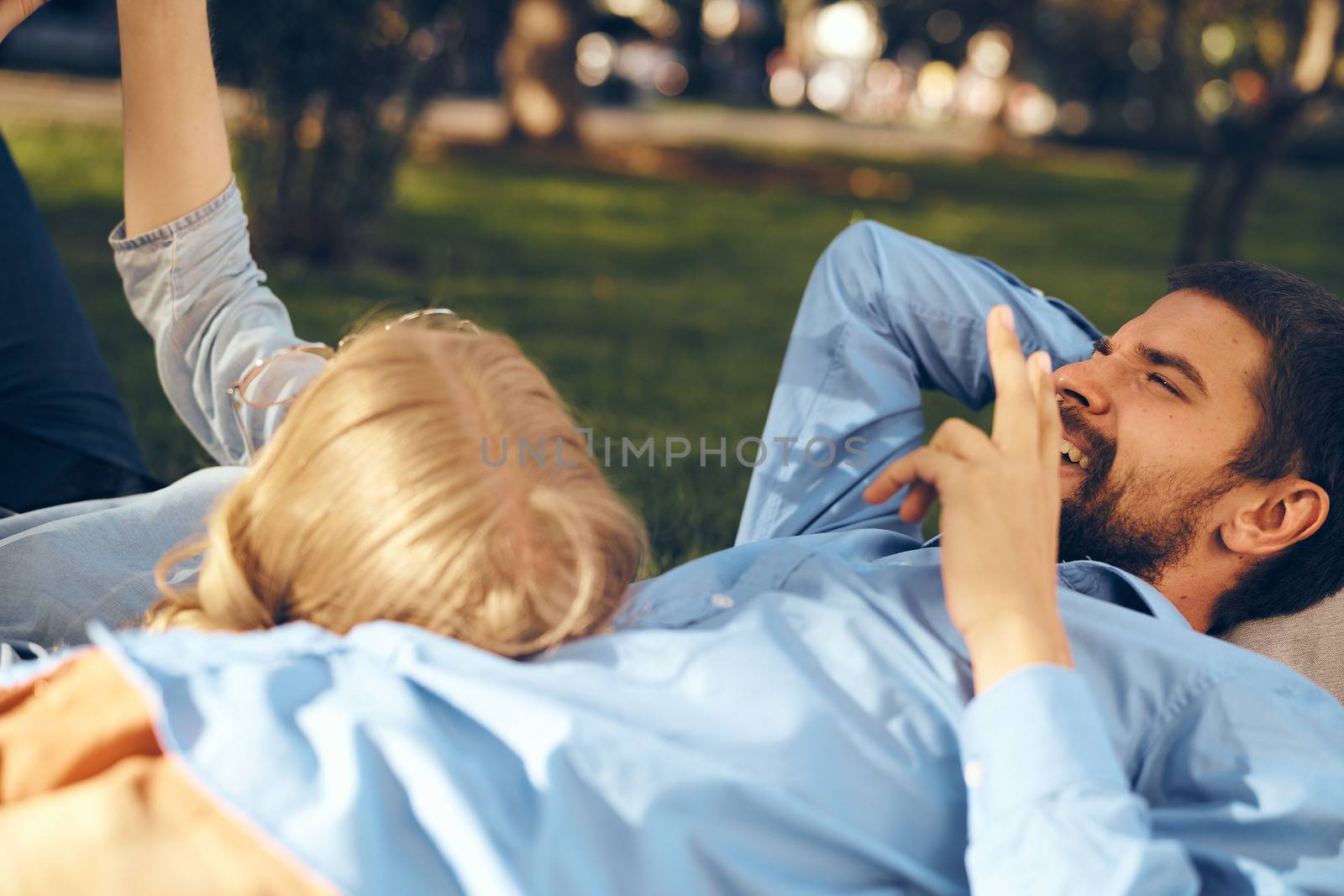 A man and a woman lie in the park on the grass with a phone in their hands rest communication by SHOTPRIME