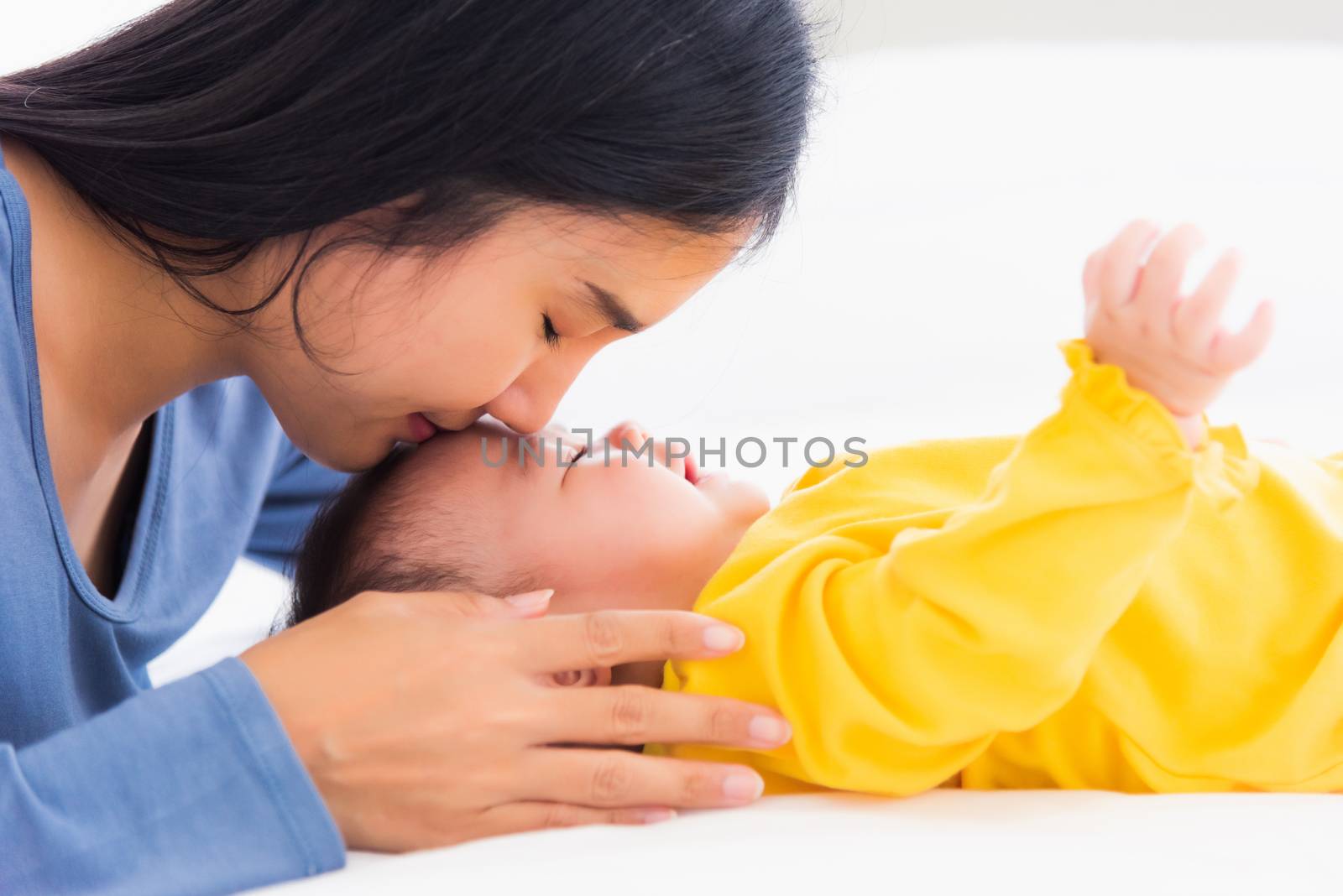 Portrait of beautiful young Asian mother kissing her infant newborn baby in a white bed, The mom loves his child, Healthcare and medical and mother day concept