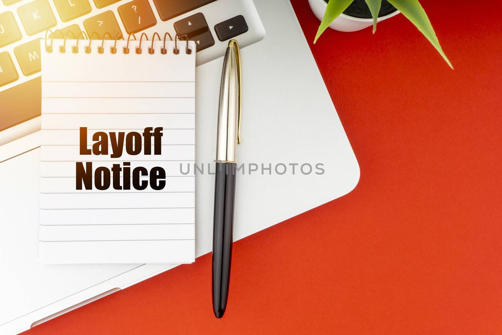 LAYOFF NOTICE text with notepad, laptop, fountain pen and decorative plant on red background. by silverwings