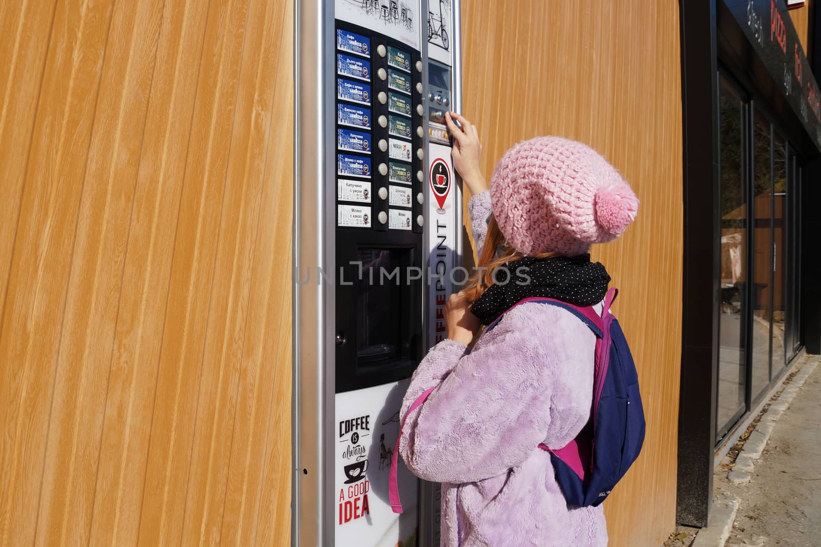 Teen girl in a medical mask buys a drink from a vending machine on the street by Annado