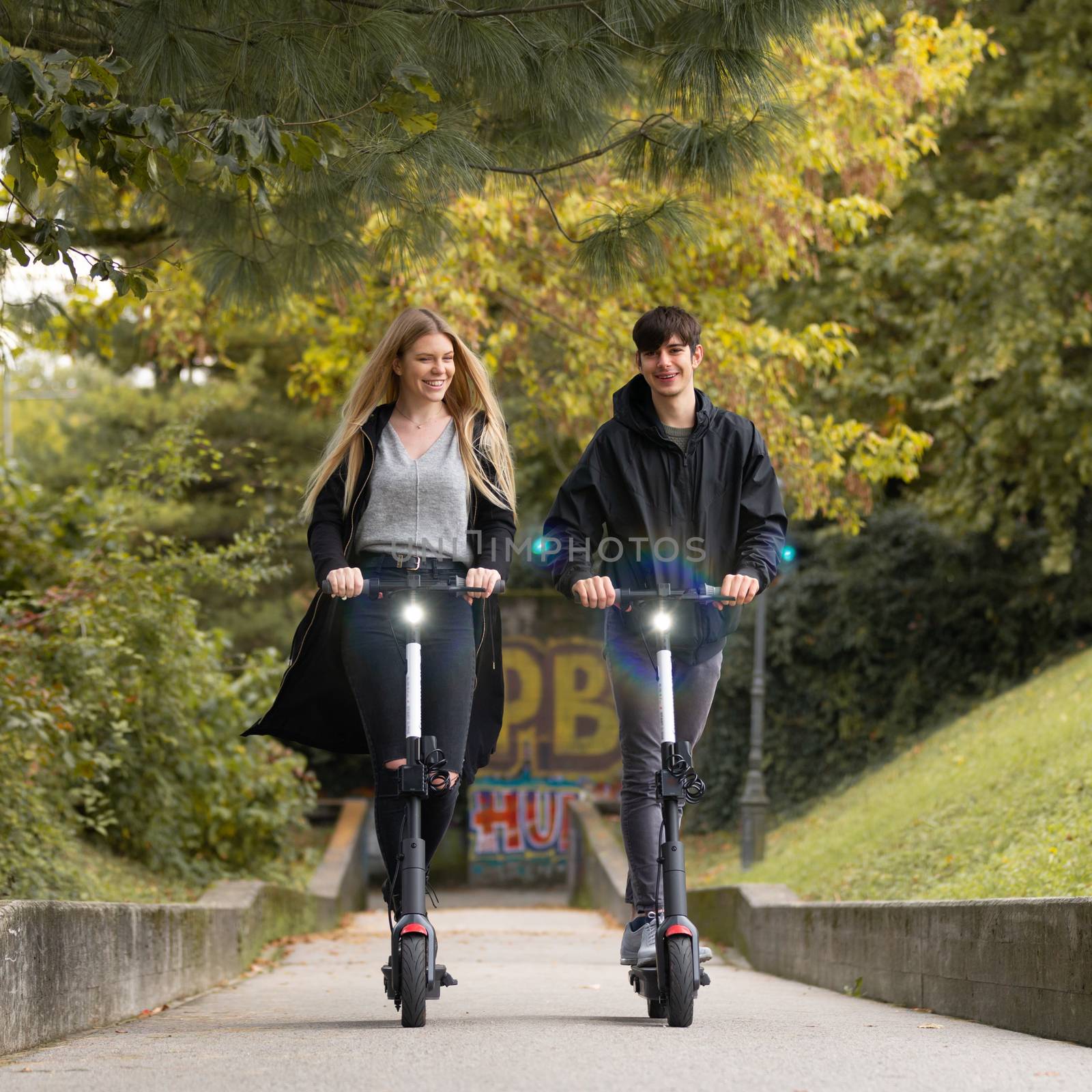 Trendy fashinable teenagers riding public rental electric scooters in urban city park. New eco-friendly modern public city transport in Ljubljana, Slovenia.