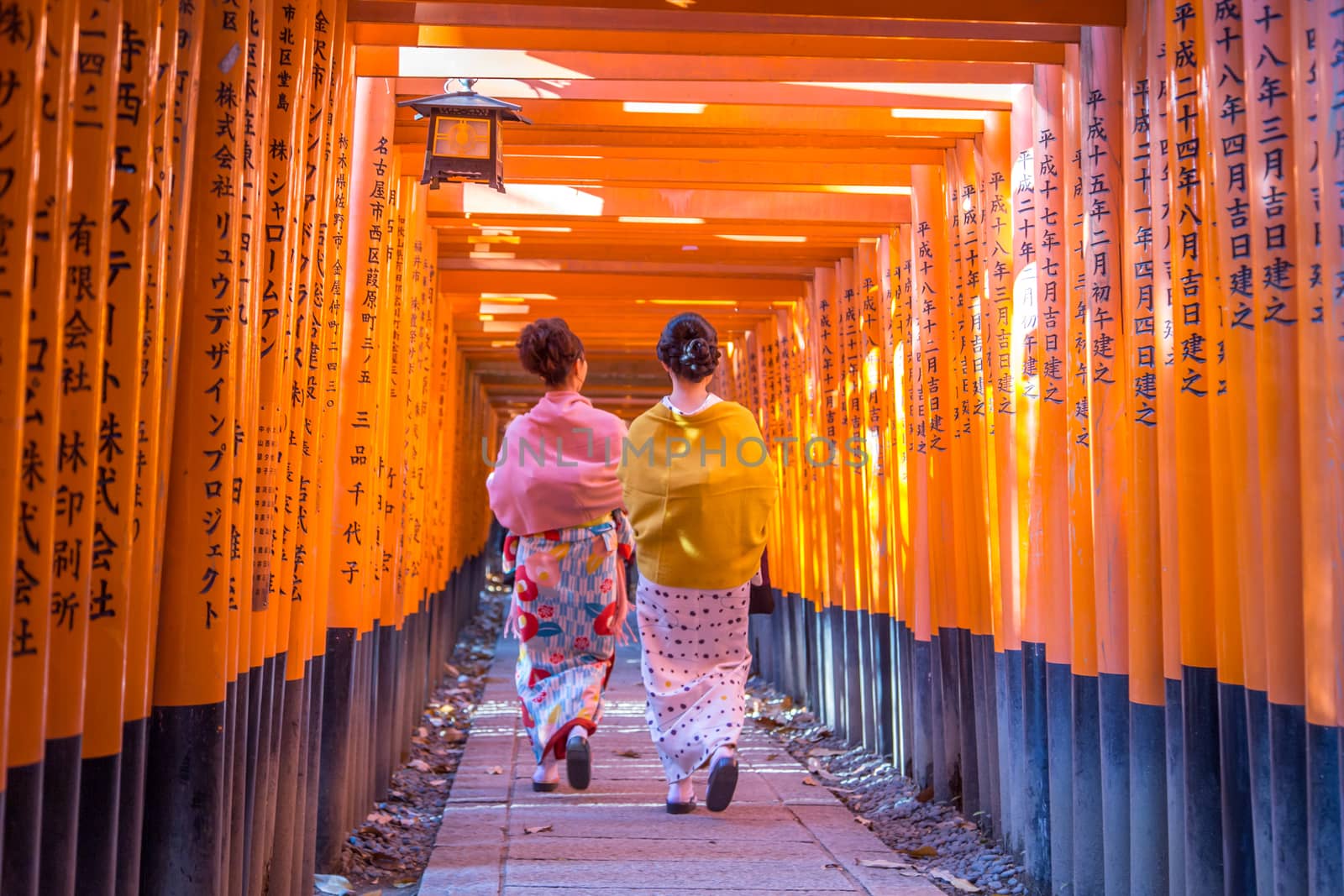 Kyoto, Japan - December 13, 2014: Two geishas walking through orange gates called torii at the Fushimi Inari Shrine