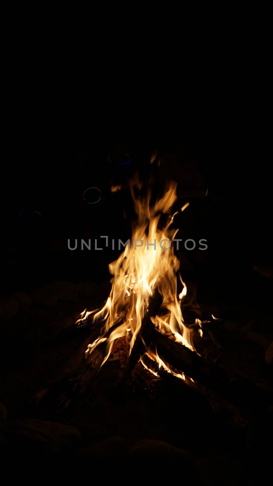 A fire is burning. People make marshmallows. Sparks fly from the fire. The embers glow. People enjoy the warmth, have a picnic and sit around the fire. They throw wood on the fire. Outdoor recreation.